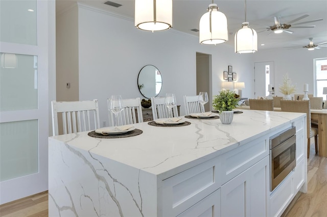 kitchen with stainless steel microwave, hanging light fixtures, white cabinets, and light stone counters