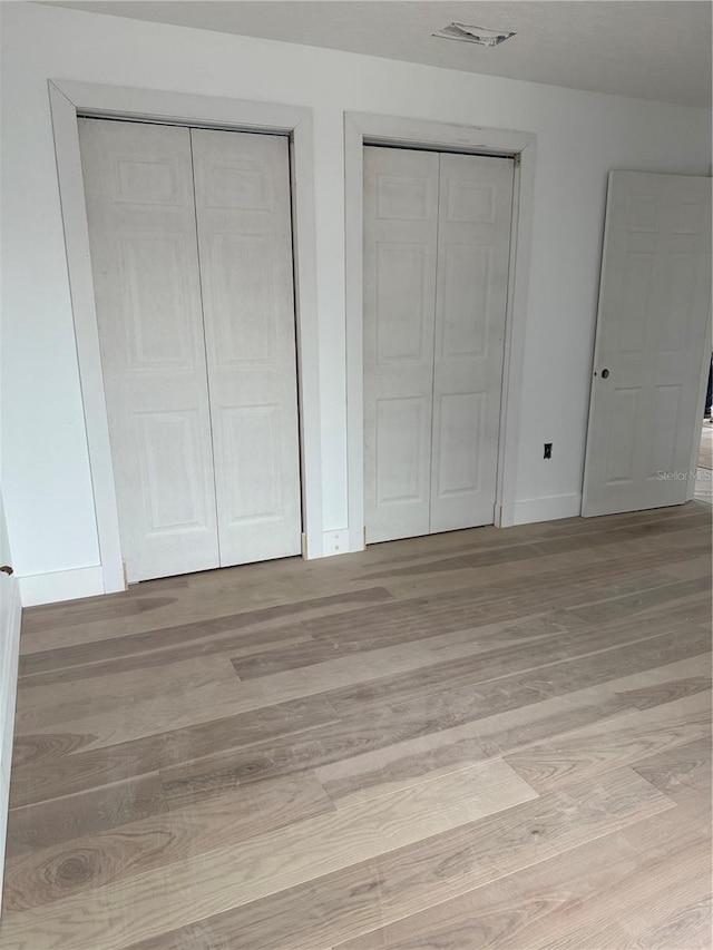 unfurnished bedroom with light hardwood / wood-style floors and two closets