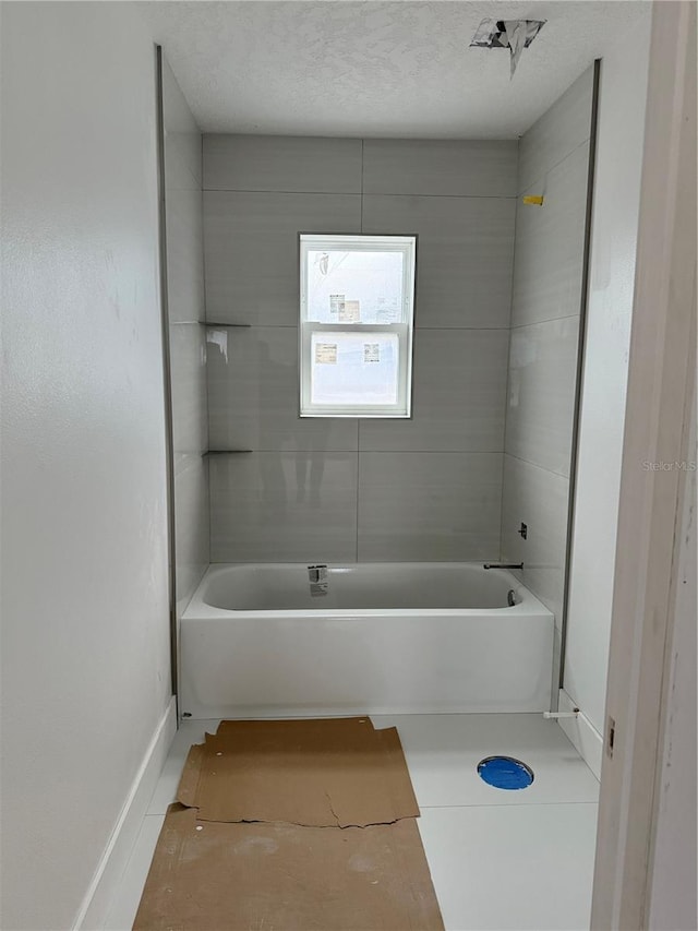 bathroom with a textured ceiling, tile patterned floors, and tiled shower / bath combo