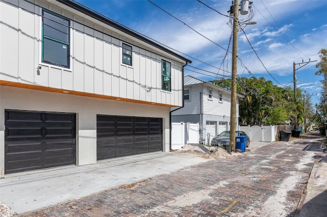 view of side of home featuring an attached garage, fence, decorative driveway, board and batten siding, and stucco siding