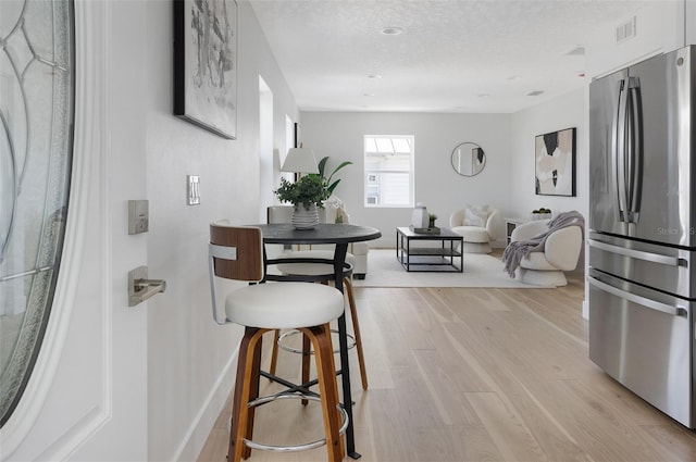 dining space featuring visible vents, a textured ceiling, light wood-style flooring, and baseboards