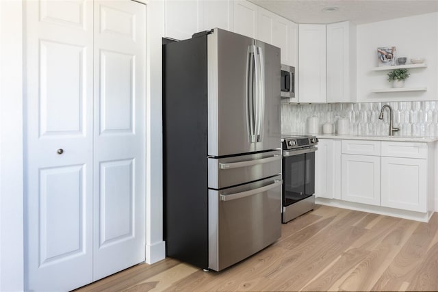 kitchen featuring light wood-style flooring, a sink, light countertops, appliances with stainless steel finishes, and open shelves