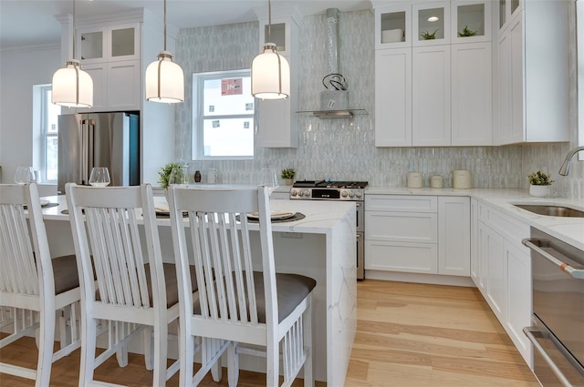 kitchen with a sink, appliances with stainless steel finishes, light stone countertops, wall chimney exhaust hood, and light wood finished floors