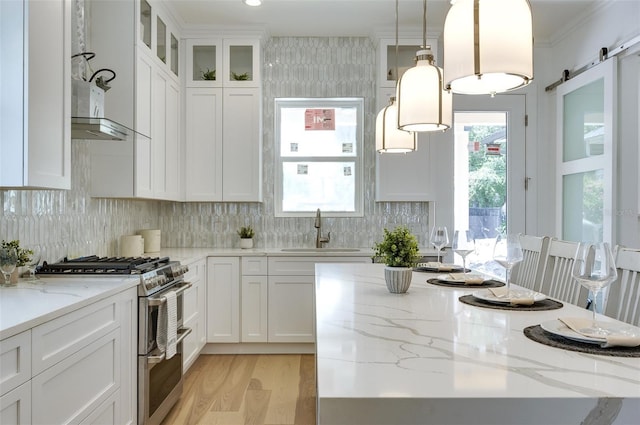 kitchen featuring a barn door, decorative backsplash, range with two ovens, white cabinetry, and a sink