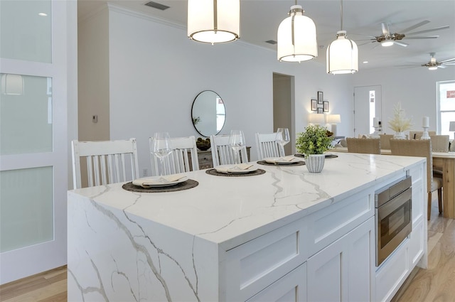 kitchen with pendant lighting, light wood finished floors, stainless steel microwave, open floor plan, and a kitchen island