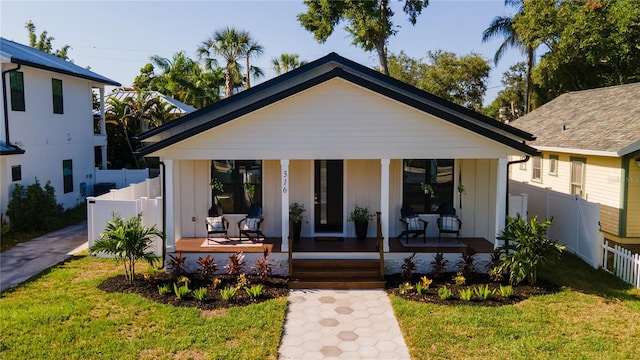 bungalow featuring a porch, board and batten siding, a front lawn, and fence