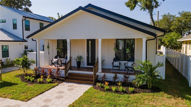 view of front of home with board and batten siding, a front yard, covered porch, and fence