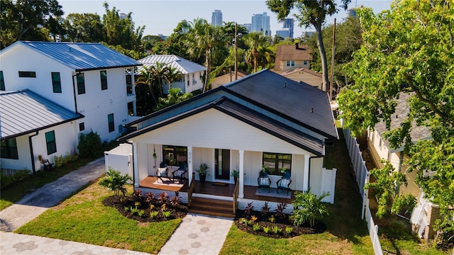 view of front of home with metal roof, covered porch, fence, driveway, and a standing seam roof