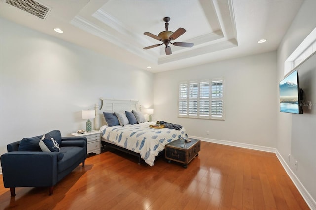 bedroom with hardwood / wood-style flooring, a raised ceiling, ceiling fan, and crown molding