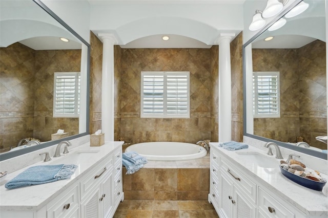 bathroom featuring vanity, a relaxing tiled tub, tile walls, and a wealth of natural light