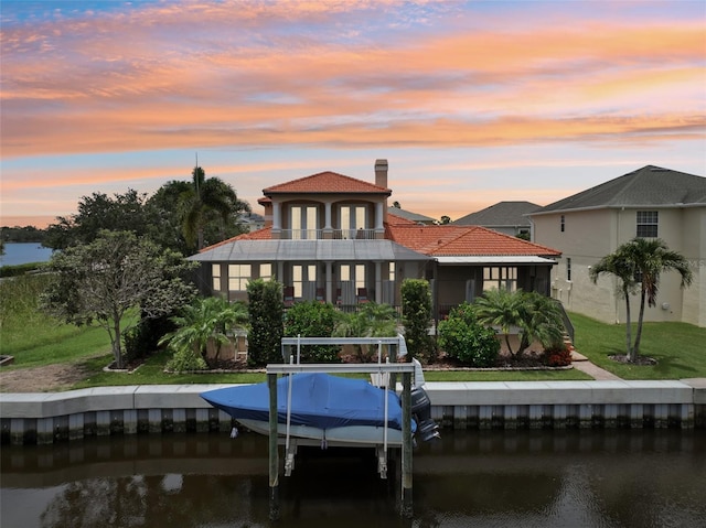 back house at dusk featuring a lawn, a balcony, and a water view