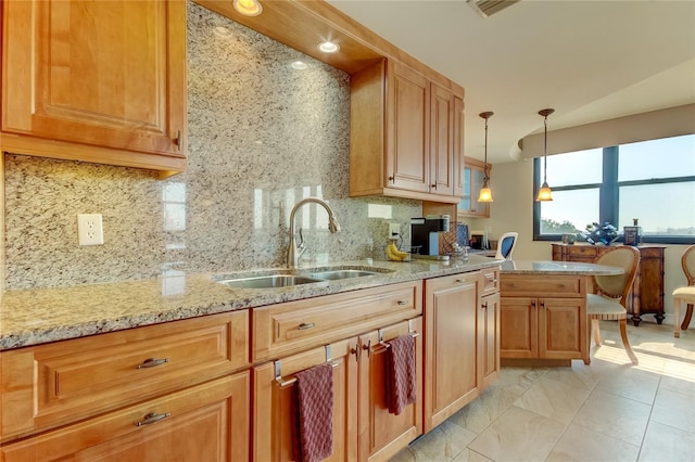 kitchen featuring pendant lighting, decorative backsplash, light stone counters, and sink