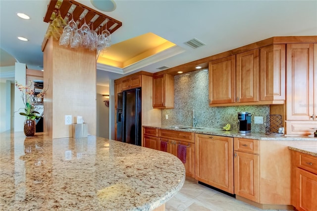 kitchen with light stone countertops, black fridge with ice dispenser, decorative backsplash, and sink