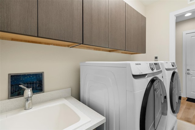 washroom with light hardwood / wood-style flooring, sink, washer and clothes dryer, and cabinets