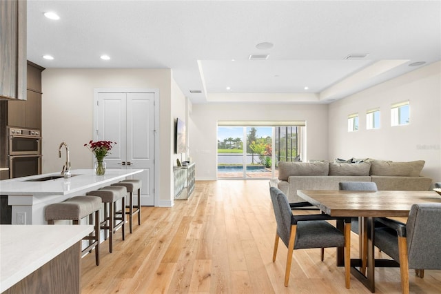 dining room with sink, light wood-type flooring, and a tray ceiling