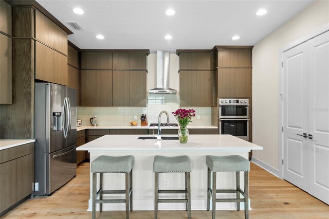 kitchen with stainless steel appliances, a kitchen breakfast bar, wall chimney exhaust hood, and light wood-type flooring