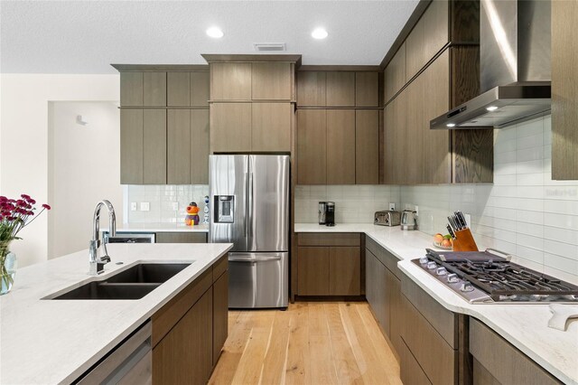 kitchen with sink, stainless steel appliances, tasteful backsplash, wall chimney exhaust hood, and light wood-type flooring