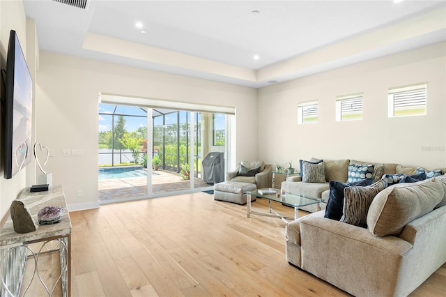 living room with a raised ceiling, a healthy amount of sunlight, and light hardwood / wood-style floors