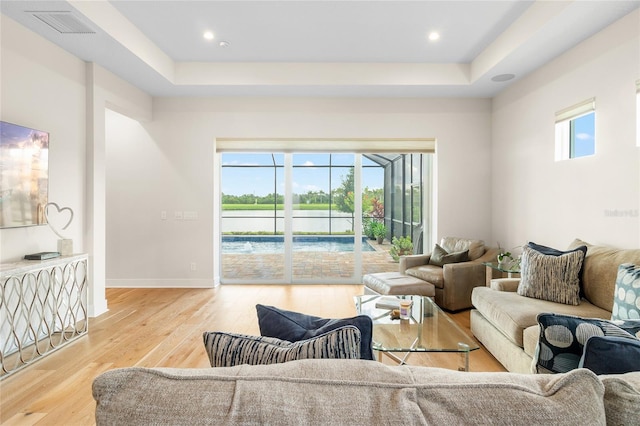 living room with a tray ceiling and light wood-type flooring