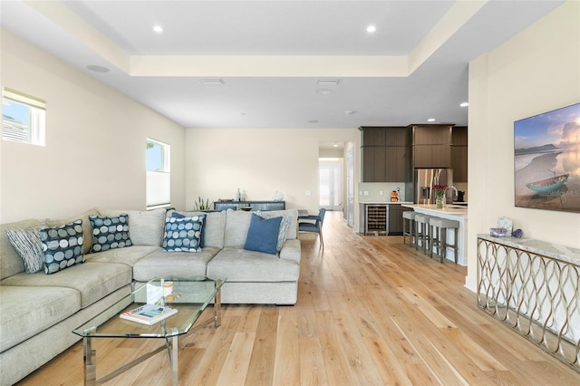 living room with wine cooler, sink, a raised ceiling, and light hardwood / wood-style floors