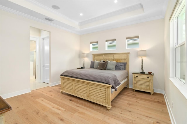 bedroom with ornamental molding, light hardwood / wood-style floors, and a tray ceiling