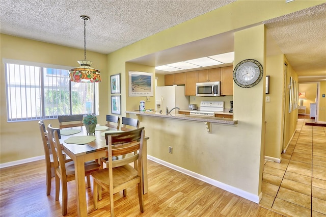 dining space featuring a textured ceiling, light wood-type flooring, and baseboards