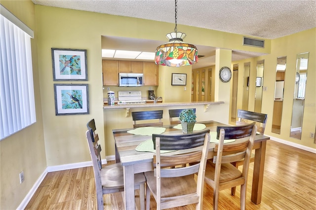 dining area featuring visible vents, a textured ceiling, light wood-type flooring, and baseboards