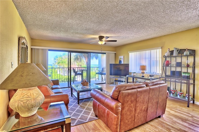 living room featuring ceiling fan, light wood-type flooring, and a textured ceiling