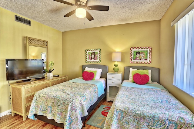 bedroom with multiple windows, wood-type flooring, a textured ceiling, and ceiling fan