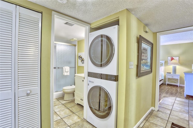 washroom featuring stacked washing maching and dryer, a textured ceiling, and light tile patterned floors