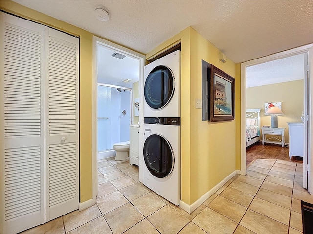7532 Bayshore Dr Unit 205, Treasure Island, FL 33706 - laundry room featuring stacked washer and clothes dryer, light tile patterned flooring, a textured ceiling, and baseboards
