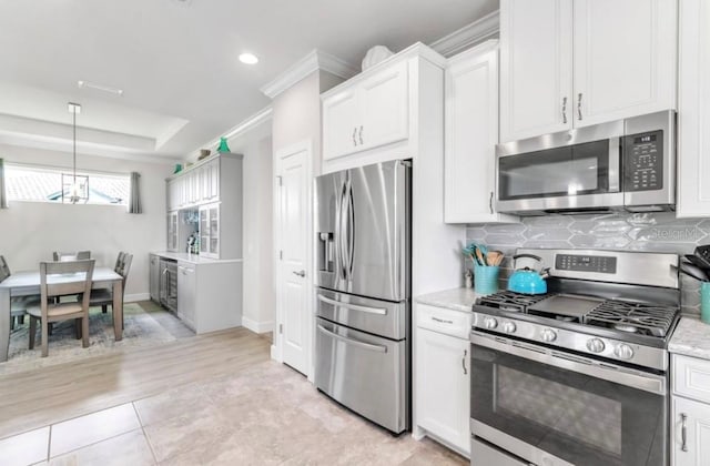 kitchen with light stone counters, stainless steel appliances, a raised ceiling, and white cabinets