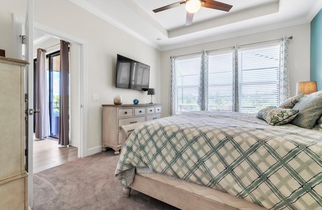 bedroom featuring ceiling fan, ornamental molding, a tray ceiling, and light colored carpet