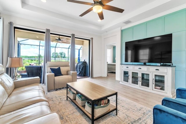 living room with a raised ceiling, crown molding, and light hardwood / wood-style flooring