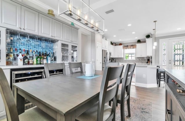 dining room with bar, crown molding, beverage cooler, and light wood-type flooring