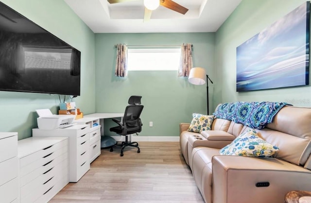 home office with ceiling fan, light hardwood / wood-style floors, and a tray ceiling