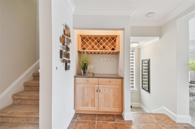 bar with a textured ceiling, light brown cabinetry, and ornamental molding