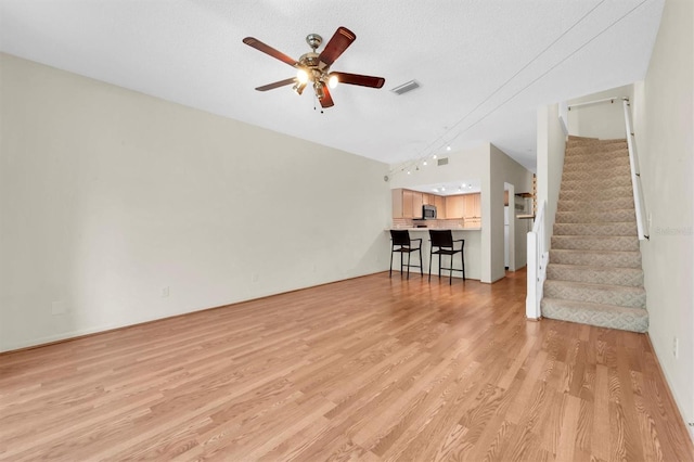 unfurnished living room with ceiling fan, lofted ceiling, a textured ceiling, and light hardwood / wood-style flooring