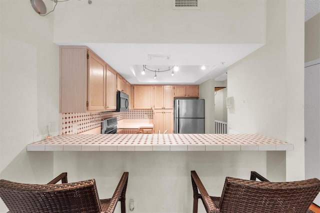 kitchen featuring a breakfast bar area, tile countertops, stainless steel fridge, and stove