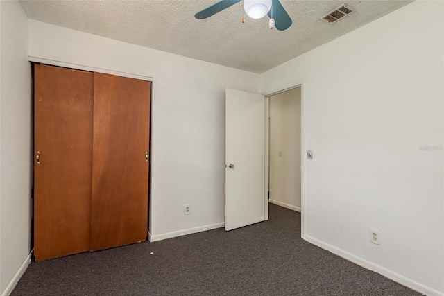 unfurnished bedroom featuring dark colored carpet, a textured ceiling, a closet, and ceiling fan