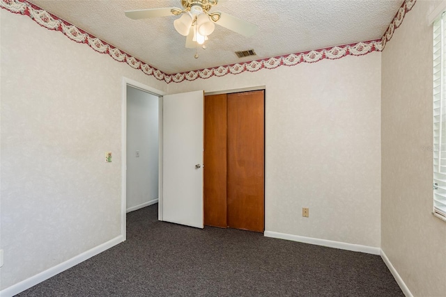 unfurnished bedroom with ceiling fan, a closet, dark carpet, and a textured ceiling