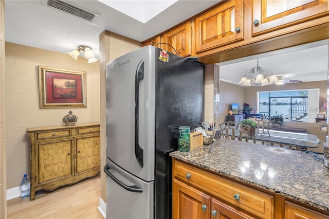 kitchen featuring stainless steel refrigerator, dark stone countertops, light hardwood / wood-style flooring, and an inviting chandelier