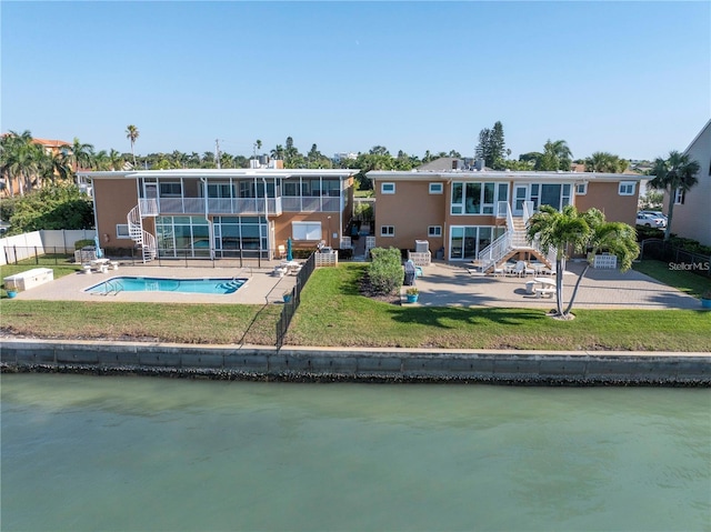 rear view of property featuring a water view, a sunroom, a patio, a fenced in pool, and a lawn