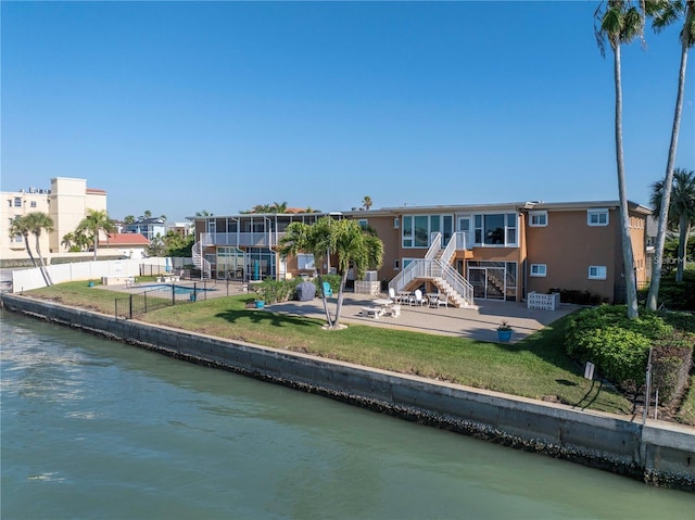 back of property with a lawn, a patio area, and a water view