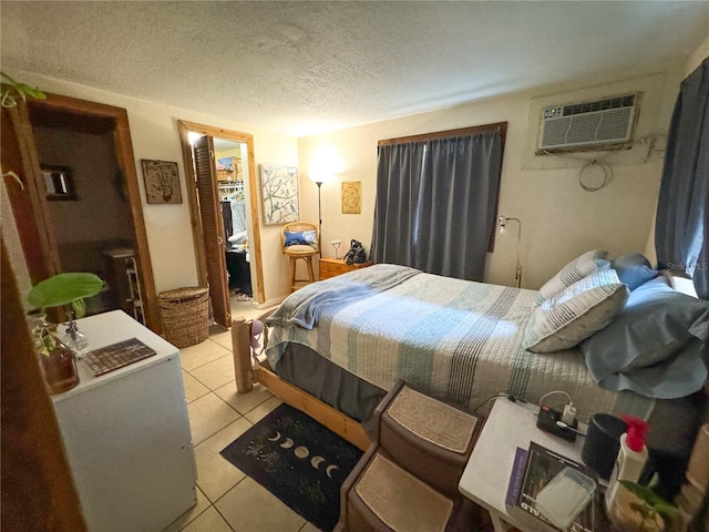 bedroom with a walk in closet, a textured ceiling, light tile patterned floors, a closet, and a wall unit AC