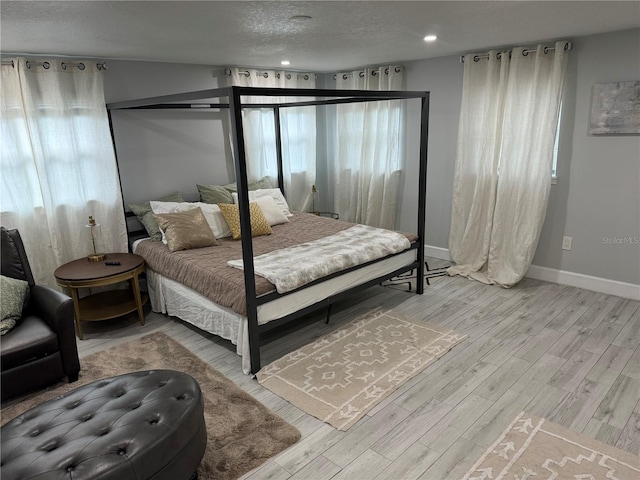 bedroom with light wood-type flooring, baseboards, a textured ceiling, and recessed lighting