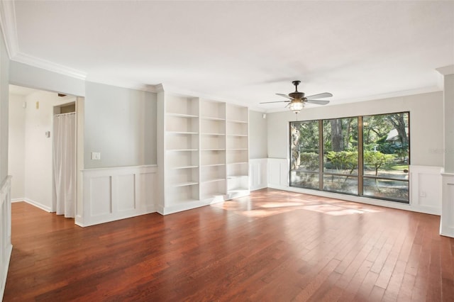 empty room with built in shelves, dark hardwood / wood-style floors, ceiling fan, and crown molding