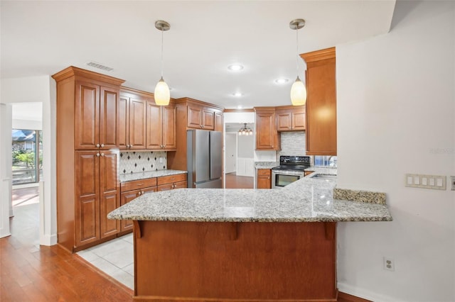 kitchen with kitchen peninsula, stainless steel appliances, hanging light fixtures, and light hardwood / wood-style flooring