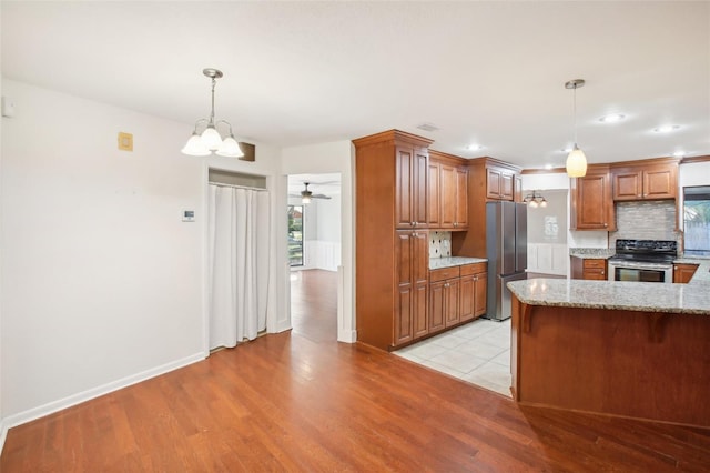 kitchen with decorative backsplash, light stone counters, stainless steel appliances, decorative light fixtures, and light hardwood / wood-style flooring