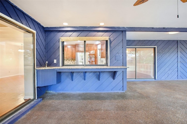 interior space featuring wood walls, ceiling fan, and dark colored carpet